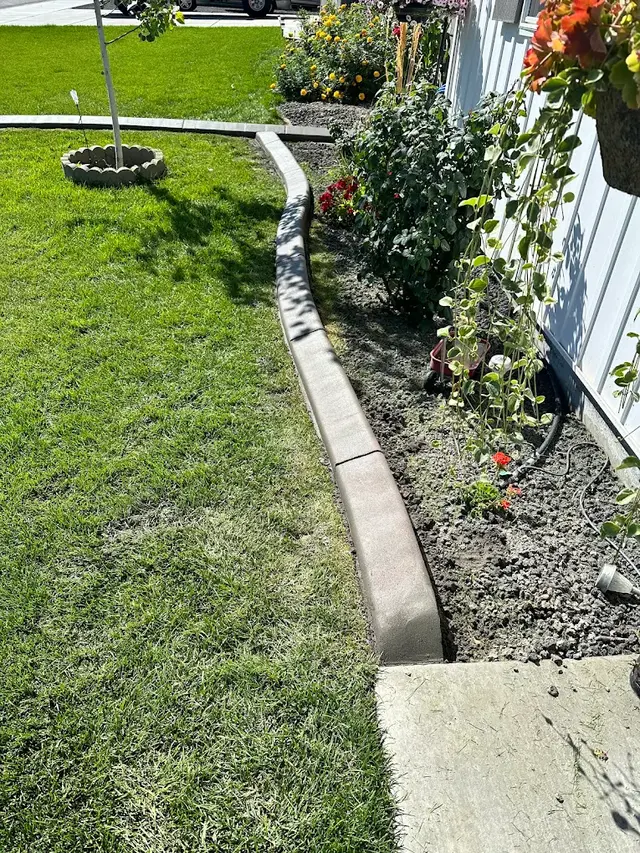 Pale stamped curbing sweeps along a rose bed and white fence beside a lawn.