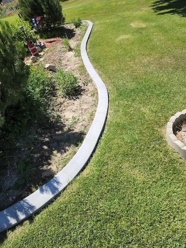 Pale patterned concrete border curves between green lawn and a mixed flower bed.