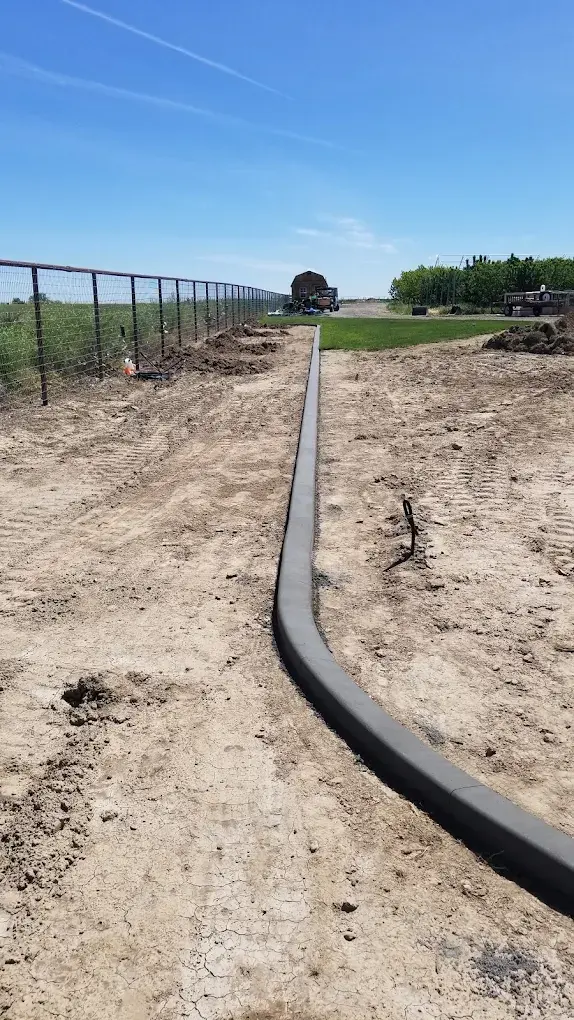Long narrow concrete border leads through a prepared rural site beneath blue sky.