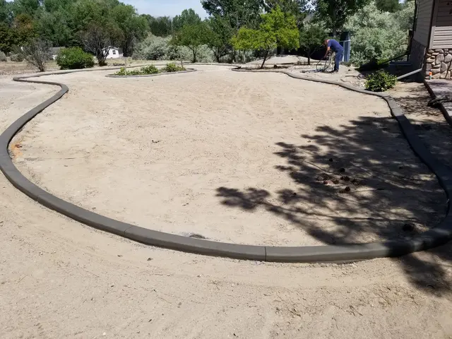 Wide newly installed gray curving lawn outline around a bare-soil yard beside a house.