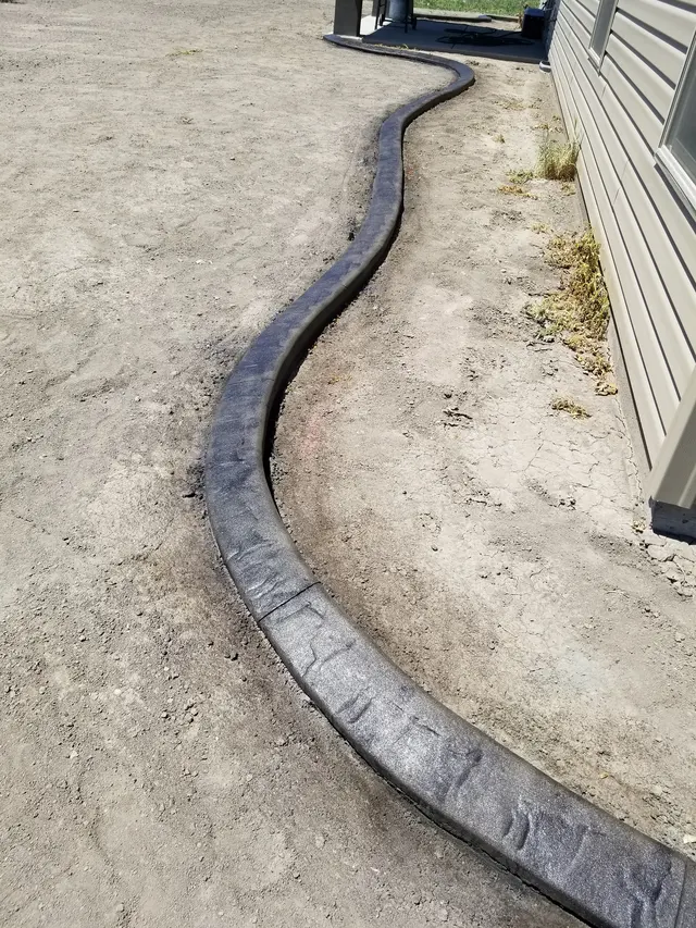 Long gray stamped curve tracing a house wall before the lawn is installed.