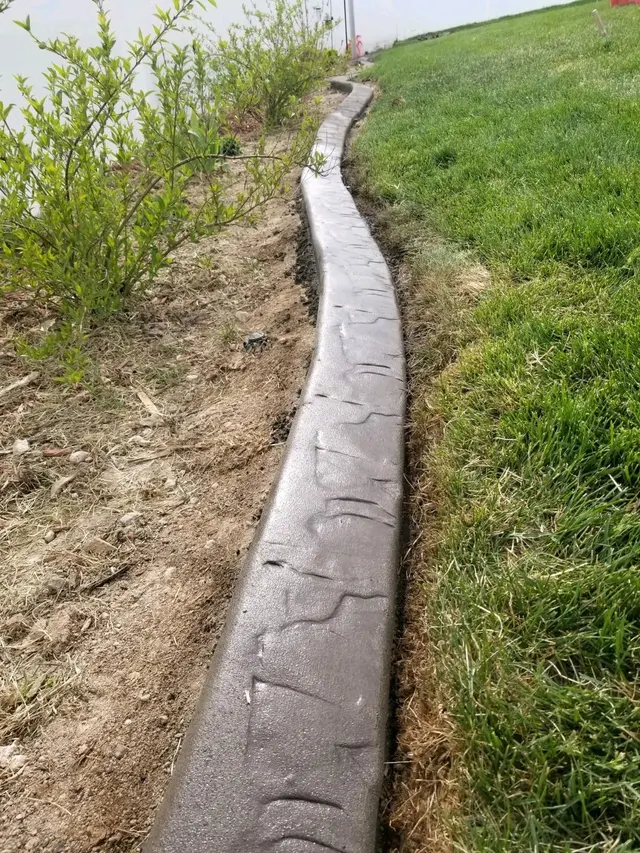 Close low-angle gray-brown stamped curb between a lawn and a planted soil bed.