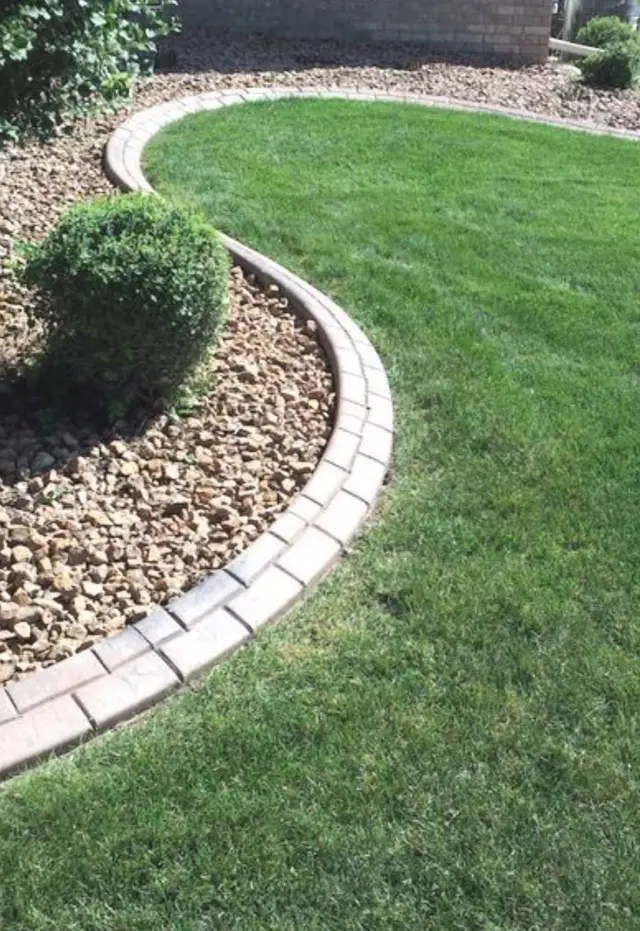 Sweeping pale stamped border around green lawn, clipped shrubs, and river-rock beds.