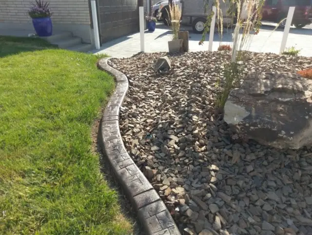 Dark stamped curve between a green lawn and a river-rock bed with a large stone.